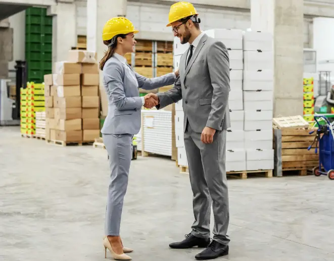 Business professionals in hard hats shaking hands in warehouse distribution center