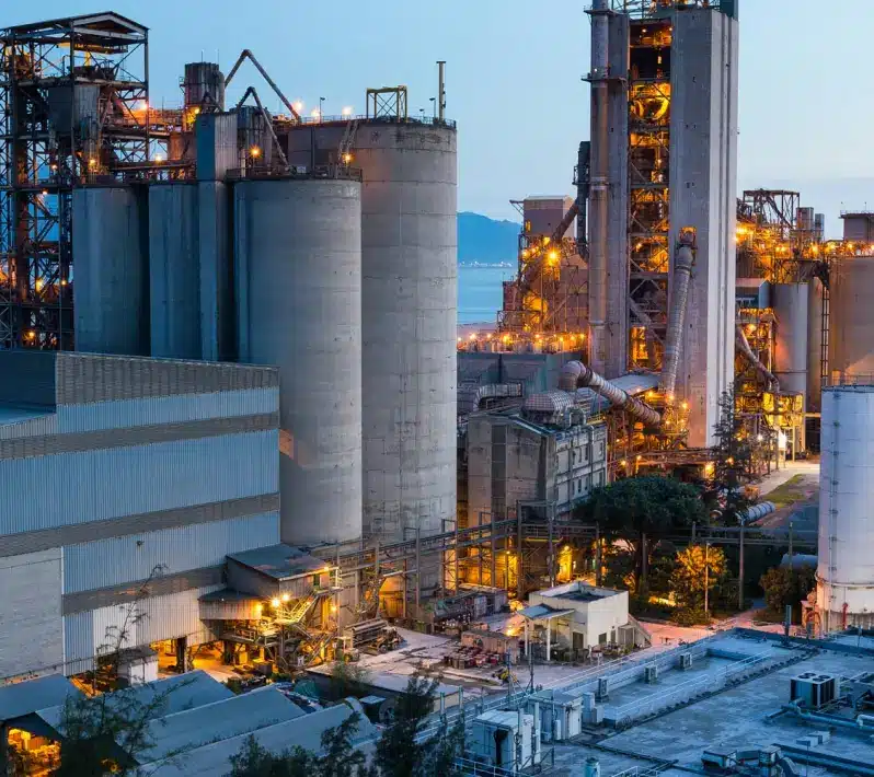 Large industrial cement manufacturing plant with tall concrete silos and processing equipment at dusk