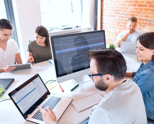 Software developers collaborating in modern office workspace with laptops and code displays