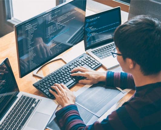 Web developer coding on multiple monitors with laptop and keyboard at desk