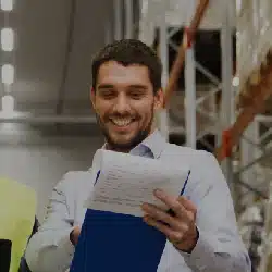 Smiling warehouse manager holding clipboard and documents in industrial storage facility