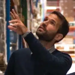 Man in navy shirt reaching up to select items from warehouse shelves