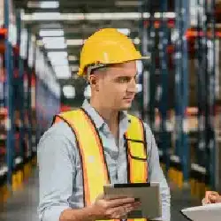 Warehouse worker in yellow safety vest and hard hat checking inventory