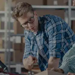 Young professional man in glasses and plaid shirt working at desk with documents