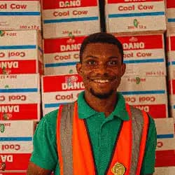 Smiling worker in green shirt and orange safety vest at warehouse with product boxes
