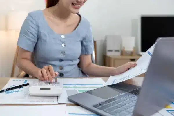 Businesswoman calculating warehouse operating costs with calculator, documents and laptop at desk