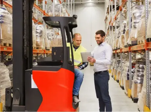 Two warehouse workers discussing operations beside red forklift in distribution center