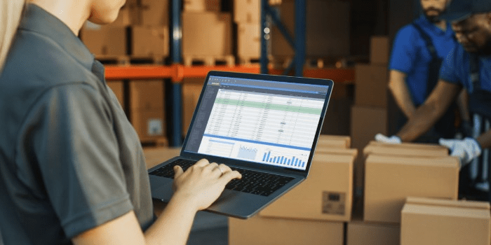 woman in warehouse holding laptop with manufacturing inventory management software