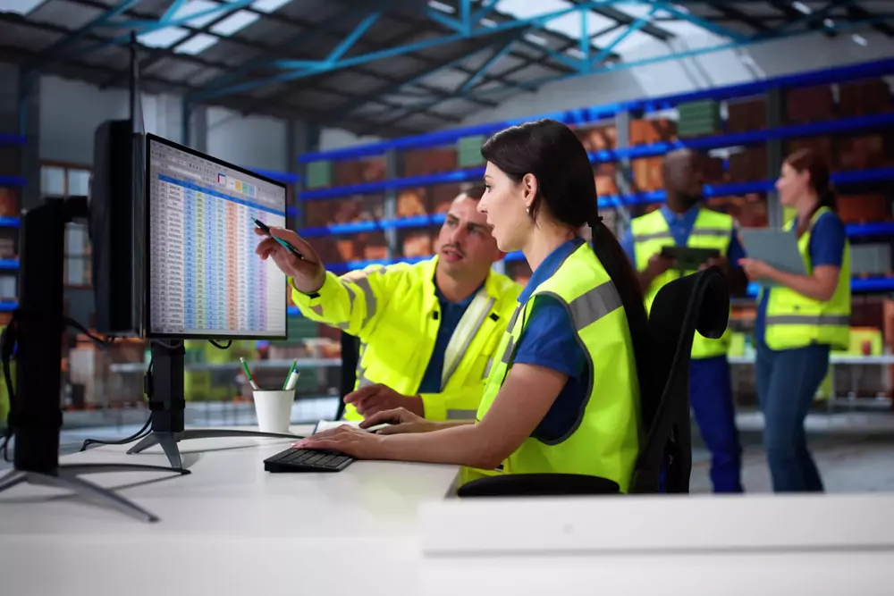 2 warehouse workers looking at a computer screen, one of them pointing at the screen