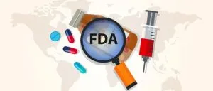 magnifying glass with FDA written on it over a bottle of pills, surrounded by pills and needle