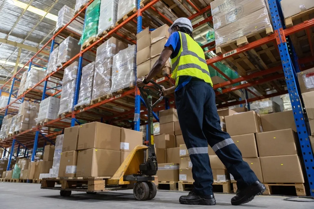 Warehouse worker in safety vest operating pallet jack in modern distribution center