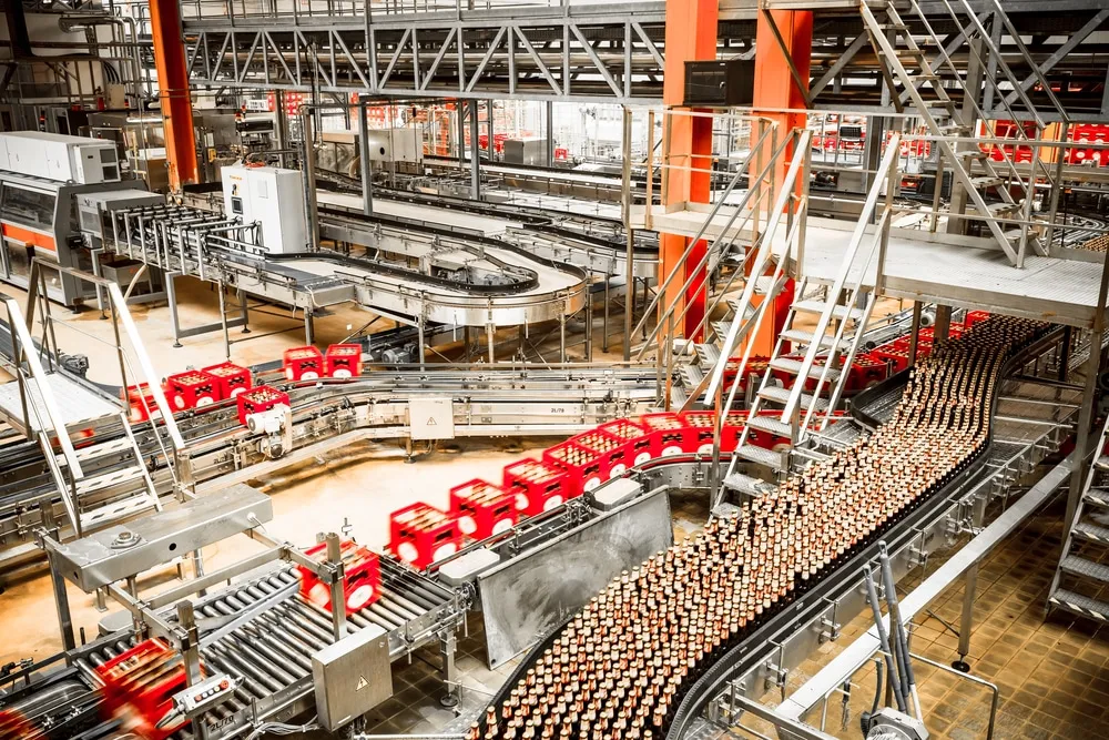 Industrial conveyor belt system transporting bottles and red packages in modern warehouse facility