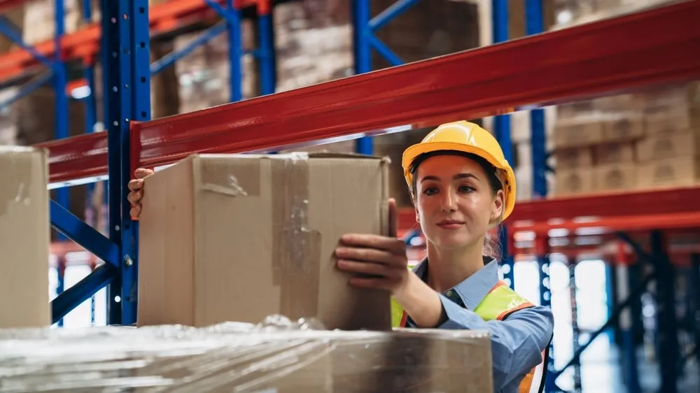 Female warehouse worker in safety helmet managing inventory on storage shelves