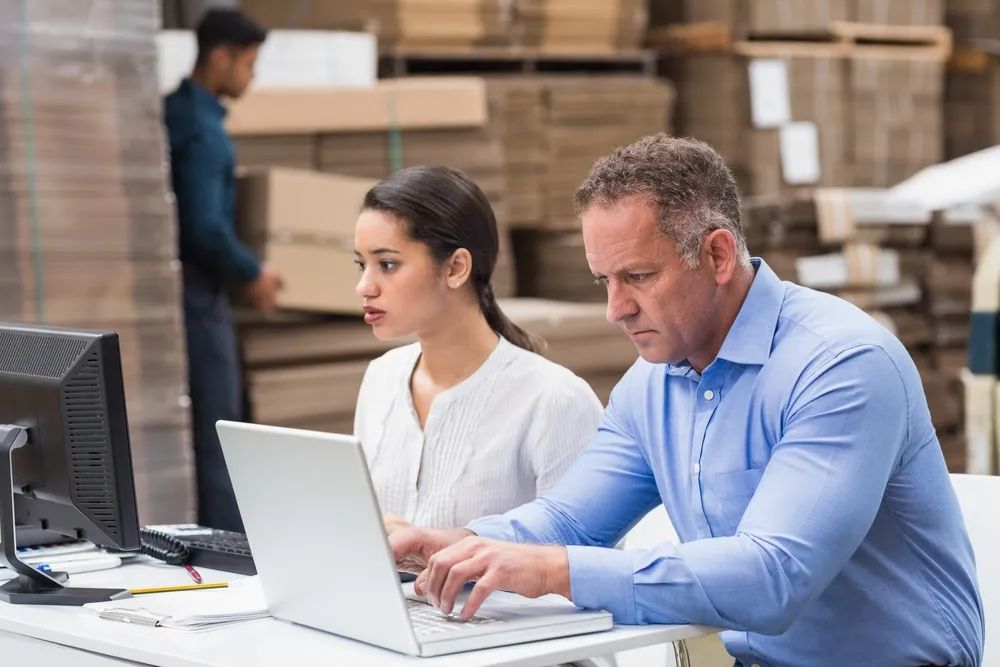 Warehouse managers analyzing demand planning data on laptops in distribution center