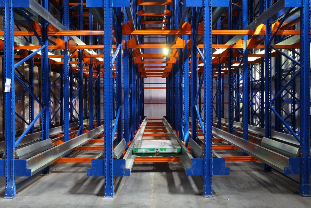 Automated storage retrieval system with blue steel racks and orange conveyor tracks in warehouse