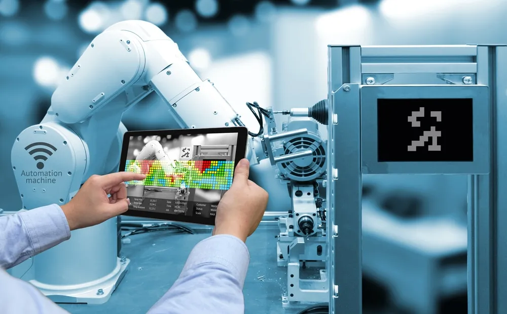 Engineer controlling industrial robot arm with tablet displaying automation data in smart factory