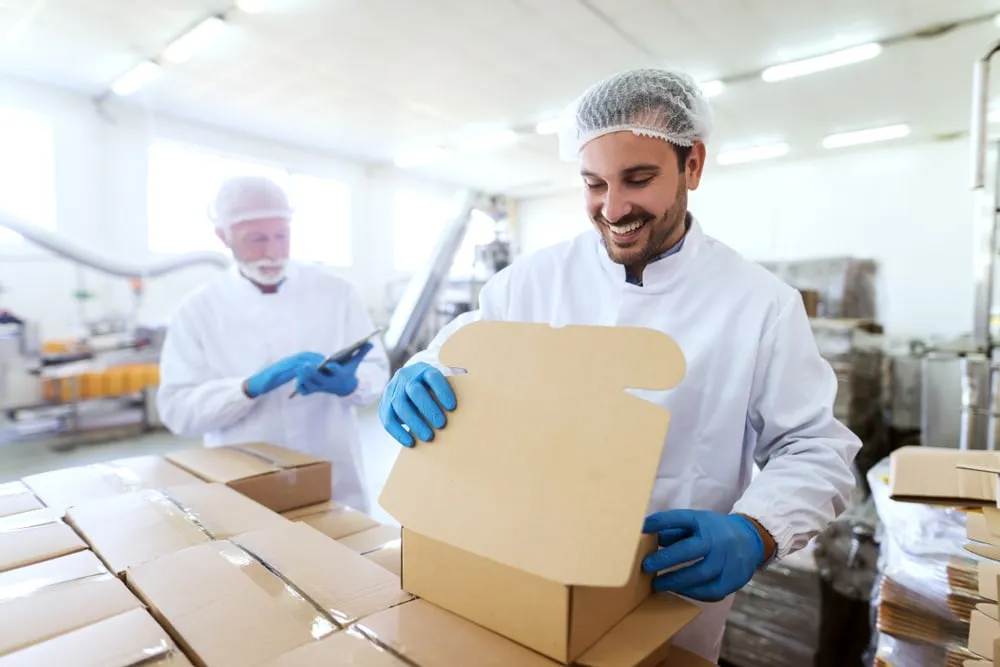 Food safety worker in white coat and hairnet packaging products in FSMA-compliant facility